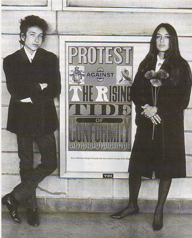 Dylan exudes a bohemian cool--
 one portrait in particular stands out--
  a faintly amused Dylan and a serious
   Joan Baez both attired in dark clothing
    standing on either side of an appropriately titled sign:
	 'Protest Against The Rising Tide Of Conformity'