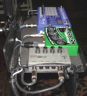 per Phillippe:
that's an Aphex Aural Exciter, voiced for acoustic instruments, a little four channel mixer, and an Adrenalinn.  The acoustic side of the Parker and the mandolin go directly into the mixer, the electric side of the Parker goes into the Adrenalinn and then that goes into the mixer.  The output of the mixer goes into the Aural Exciter which acts like a direct box with an XLR out to the board.  Viola!  What you can't see in the pictures was my arsenal of harmonicas hanging from the bottom of the board.